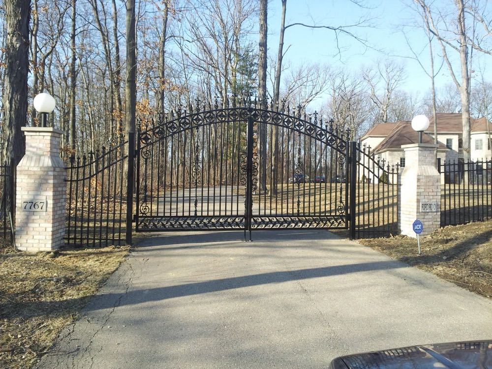 Arched black wrought iron driveway gate between pillars